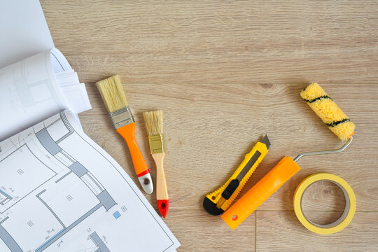 Architectural drawings and brushes, paint roller, clerical knife on wooden background. Top view. Repair housing concept.