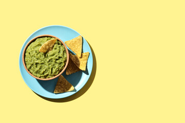 Mexican guacamole with nacho chip in wooden bowl on yellow background. Top view. Copy space