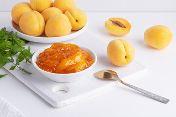 Apricot jam in a glass bowl, fresh apricots in a basket on a light wooden background