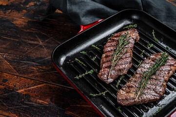 Fried denver beef meat steak with thyme in a grill skillet. Wooden background. Top view. Copy space