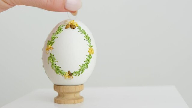 close-up of an embroidered egg on the eggshell of goose eggs female hand slowly puts it on a wooden stand on white background krashenka drawings ornaments scenery easter celebration