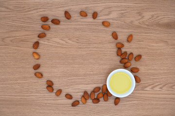 Almond oil in bowl and group of almond nuts on wooden texture background. Almond oil with almond seeds. Top view.