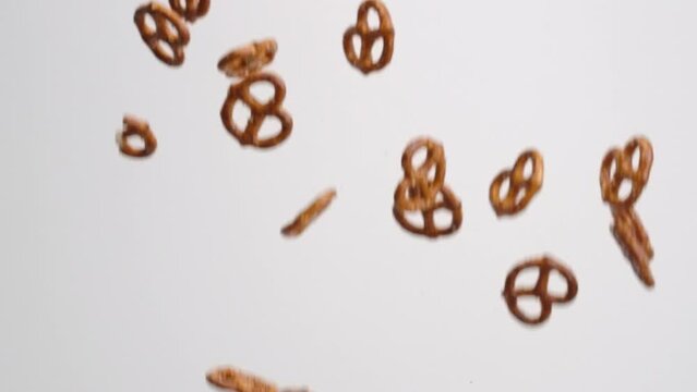 Salty twisted pretzel snack crackers raining down and bouncing on white backdrop in slow motion