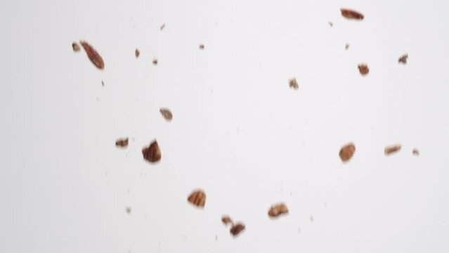 Whole brown roasted and salted pecan nuts raining down on white backdrop in slow motion