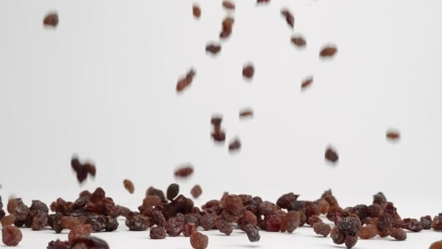 Wrinkly dried red grape raisins falling onto white table top and bouncing into a pile in slow motion