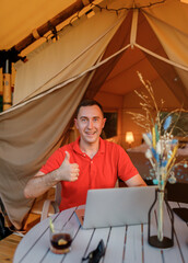 Obraz na płótnie Canvas Happy man freelance programmer using laptop and showing thumb up on cozy glamping tent in a summer day. Luxury camping tent for outdoor holiday and vacation. Lifestyle concept