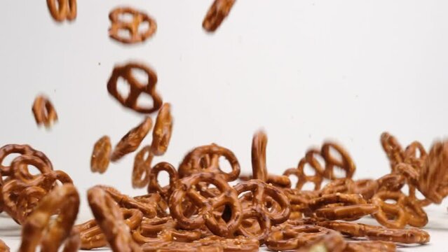 Salty twisted pretzel snack crackers falling onto white table top and bouncing around into a pile in slow motion