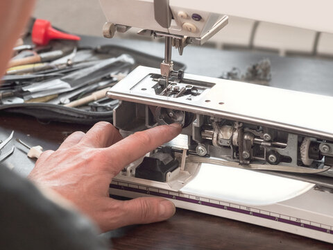 The finger of the sewing machine adjuster repairs the internal mechanism. Professional adjustment of a sewing machine in a small factory. Cleaning and repair of professional equipment.
