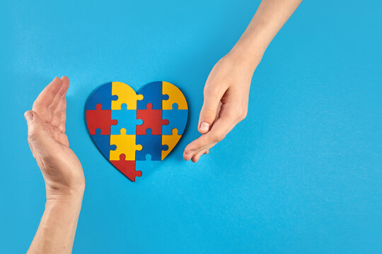 Father and autistic son hands holding jigsaw puzzle heart shape. World Autism Awareness Day