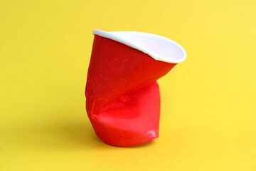 A crumpled red glass lies on a yellow background.
