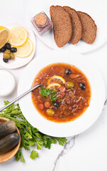 Solyanka on a white plate. Vegetable soup with olives and sausages.