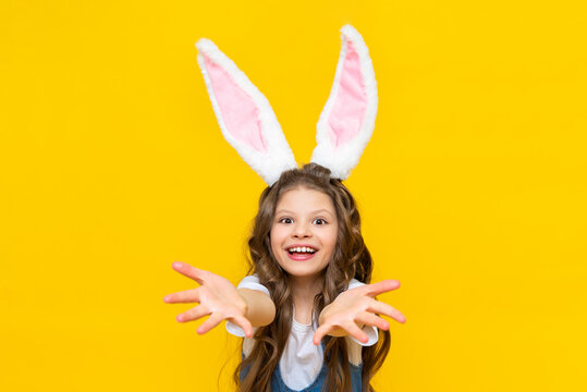 A happy little girl is enjoying Easter. Spring holiday for children. A child dressed as a rabbit with long ears. A charming lady with curly hair on a yellow isolated background.