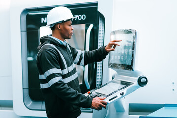 Naklejka na ściany i meble African american man specialist engineer using controller monitor for controlling robotic arm welding machine. Technician maintenance worker in safety uniform working in industry.