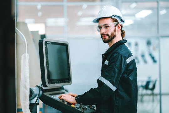 Smiling caucasian man specialist engineer using controller monitor for controlling robotic arm welding machine.