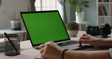 Close up shot of hands of student working with chroma key green screen laptop, using trackpad and pen with notebook in living room