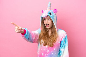 Teenager Russian girl with unicorn pajamas isolated on pink background pointing away