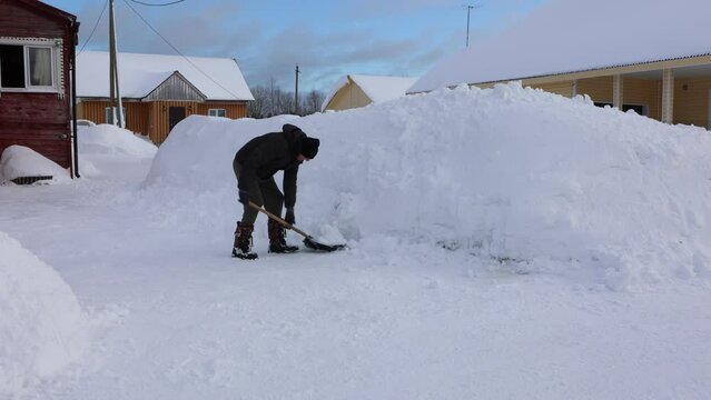 Manual snow removal with shovel, man clears snow near rural house on winter day.