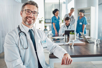 Healthcare, smile and portrait of senior doctor at desk in teaching hospital office with nurses and...