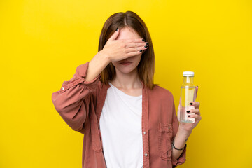 Young English woman with a bottle of water isolated on yellow background covering eyes by hands. Do not want to see something