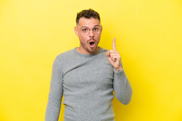 Young caucasian handsome man isolated on yellow background intending to realizes the solution while lifting a finger up