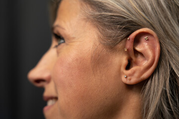 Obraz premium Profile portrait of a woman with pierced ear with four distinct jewels. Piercing concept in older people