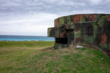 WWII bunker with camouflage pattern nestled in a green meadow on the coast of Hualien Taiwan. It's a cloudy stormy day by the sea. The sky offers copy space.