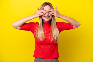 Young Uruguayan woman isolated on yellow background covering eyes by hands and smiling