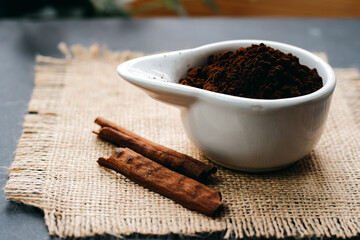 Coffee grounds in a bowl with cinnamon sticks on a burlap napkin