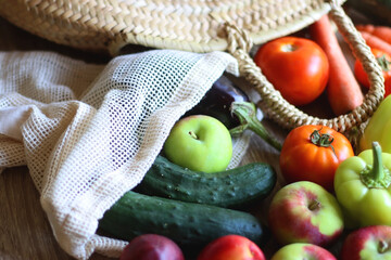 Straw bag and reusable fabric bags filled with various healthy fruit and vegetables. Wooden...