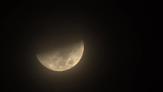 Long telephoto shot capturing half of a moon moving slowly in a dark sky