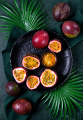Passion fruit, whole and halves, served on dark plate. Tropical fruit. Top view