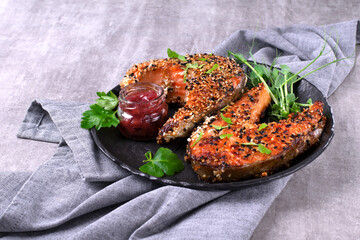 Fried trout steak served with sesame seeds, cowberry sauce and green pea microgreens on dark plate