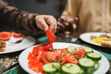 Cropped view of muslim boy taking vegetable during iftar at home.