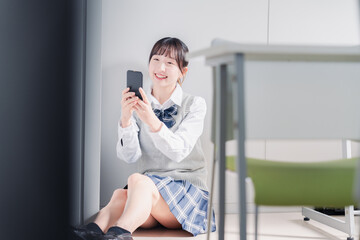 教室で笑顔でスマホを使う女子高生
