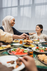 African american mother in hijab looking at daughter near ramadan dinner at home.