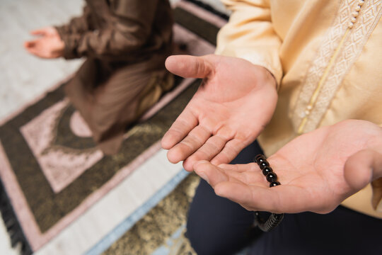Partial view of man with prayer beads praying near blurred son at home.