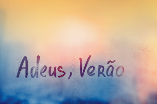 lettering Adeus Verao in Portuguese language is good bye summer in english on foggy glass on sunset window