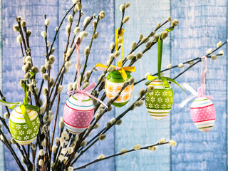 Colorful Easter eggs on willow twigs. Easter tree with festive ribbons on a blue background. Happy...