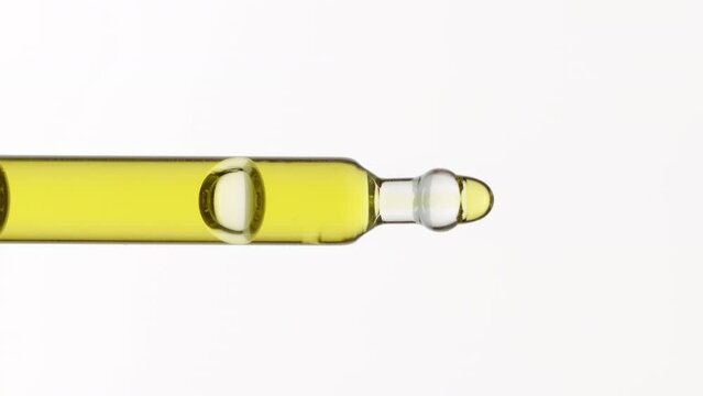 Abstract eye care serum formulation concept | Macro shot of yellow liquid is dripping from lab pipette occasionally on grey background