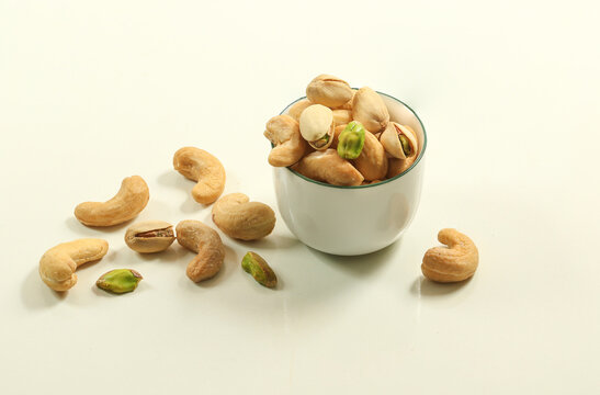 Group of hulled salty roasted cashews and pistachio nut in a white cup. Vegetarian food isolated on white