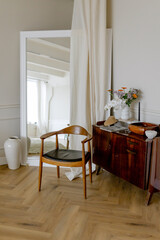 Wooden chair near the mirror and chest of drawers. Vintage style in the room.