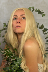 Fototapeta premium artistic portrait of an beautiful blonde woman, nymph, mermaid wrapped by flower tendrils, eucalyptus bunches off shoulder, 