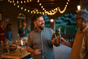 Happy man and his senior father toast with beer during family gathering on patio.