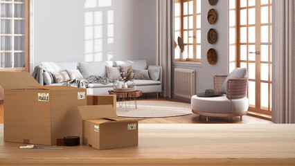 Wooden table, desk or shelf with stack of cardboard boxes over blurred view of farmhouse living room in boho style, bohemian interior design, moving house concept with copy space
