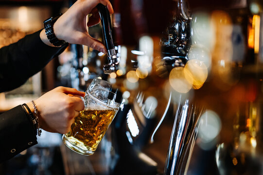 man bartender hand at beer tap pouring a draught beer in glass serving in a restaurant or pub