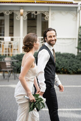 happy groom holding hand of bride in white dress with bouquet of flowers.