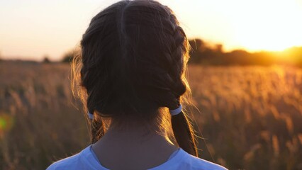 Pretty little girl stands at grass field straightening her blonde hair. Beautiful female kid turning to camera and smiling. Portrait of happy small child at summer meadow. Carefree concept. Dolly shot