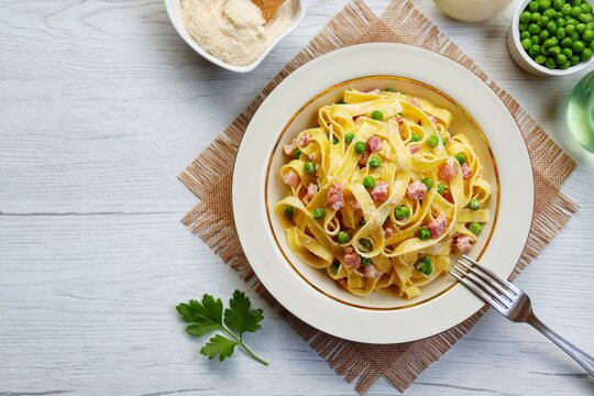 Italian Traditional Dish"Tagliatelle panna,piselli e pancetta",tagliatelle pasta with heavy cream,green peas,smoked bacon,onion,olive oil,parmesan cheeses and peppers on plate with wooden background

