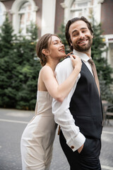 Fototapeta premium cheerful young woman in wedding dress hugging happy groom in vest.