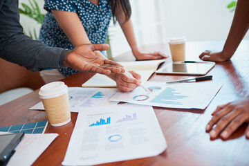 Close up of hands gesturing to financial report around conference meeting table